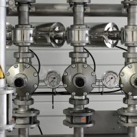 Close-up of stainless steel pipes with pressure gauges in an industrial setting.