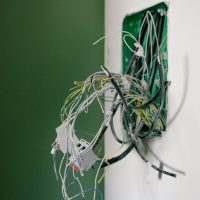 Opened power socket with various wires on white wall during repair at home
