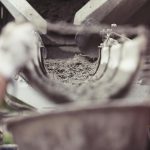 Close-up of concrete being poured from a mixer truck at a construction site with a worker's hand visible.