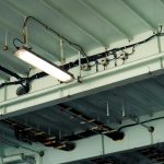 Detailed view of industrial ceiling light and wiring at a low angle in an indoor setting.