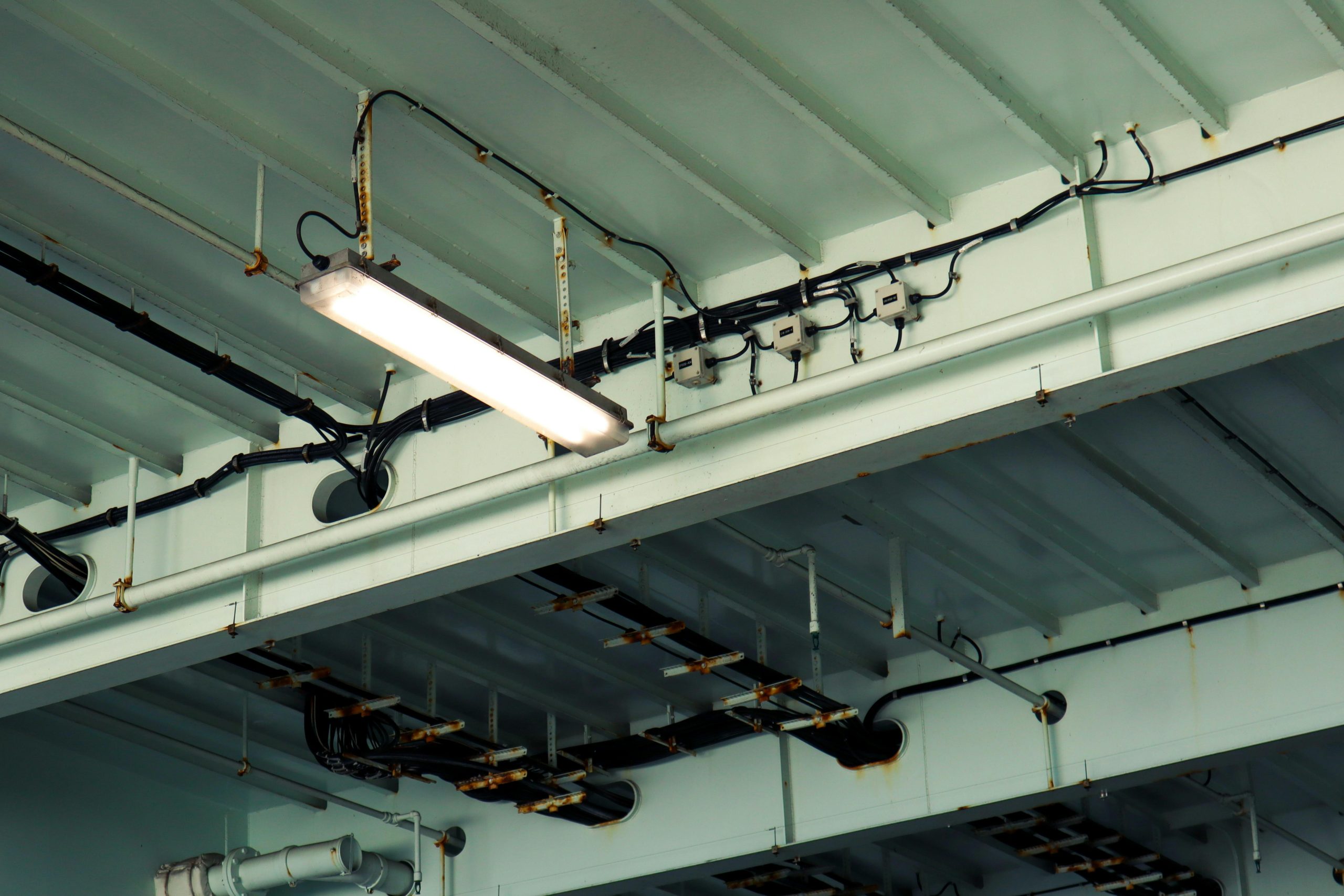 Detailed view of industrial ceiling light and wiring at a low angle in an indoor setting.