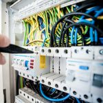 Hand of electrician working on a circuit breaker panel with colorful wires, ensuring safe electrical connections.