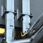 Close-up of shiny stainless steel pipes on an industrial building facade, showcasing modern technology.