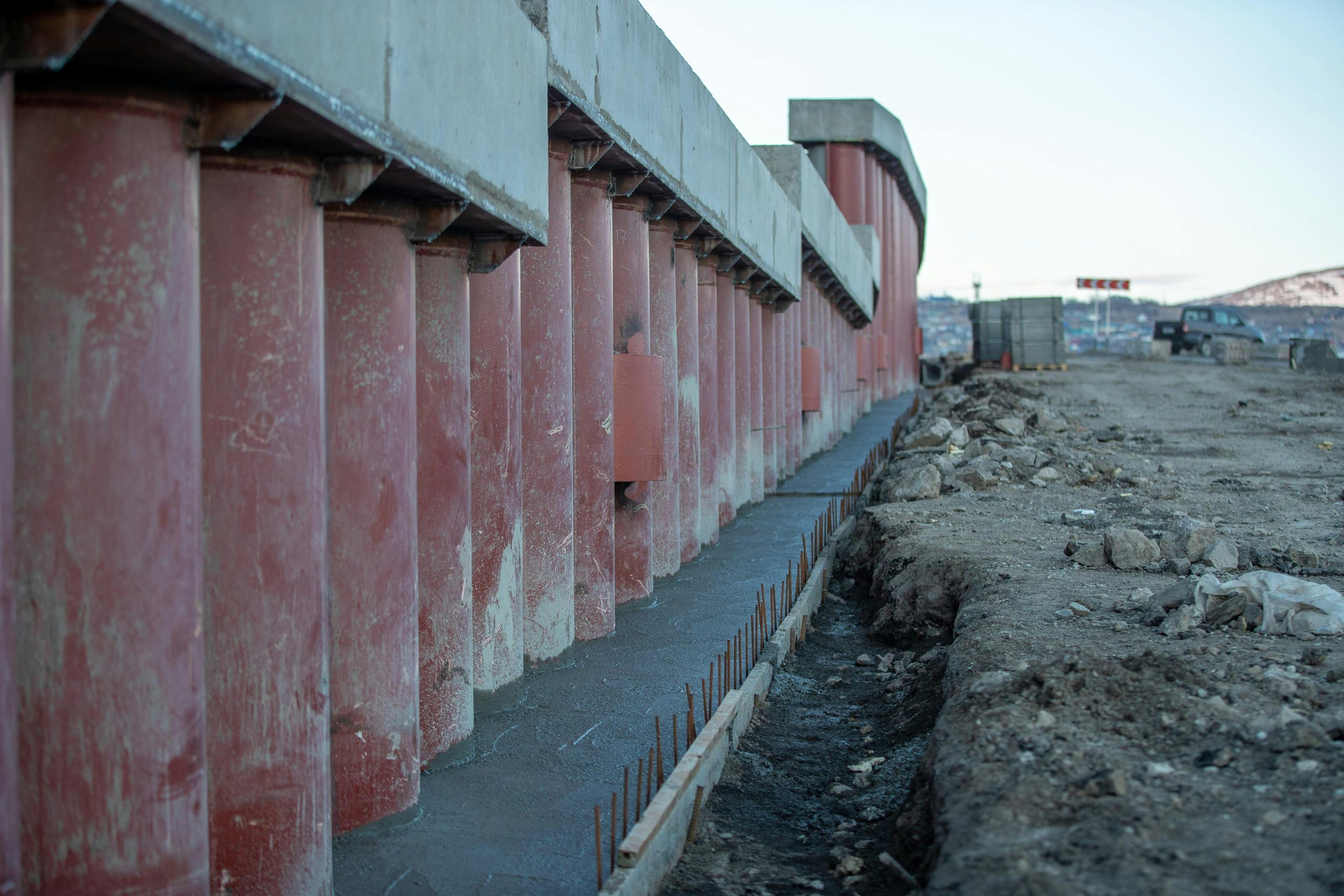 View of a construction site featuring large concrete columns, earthwork, and machinery.