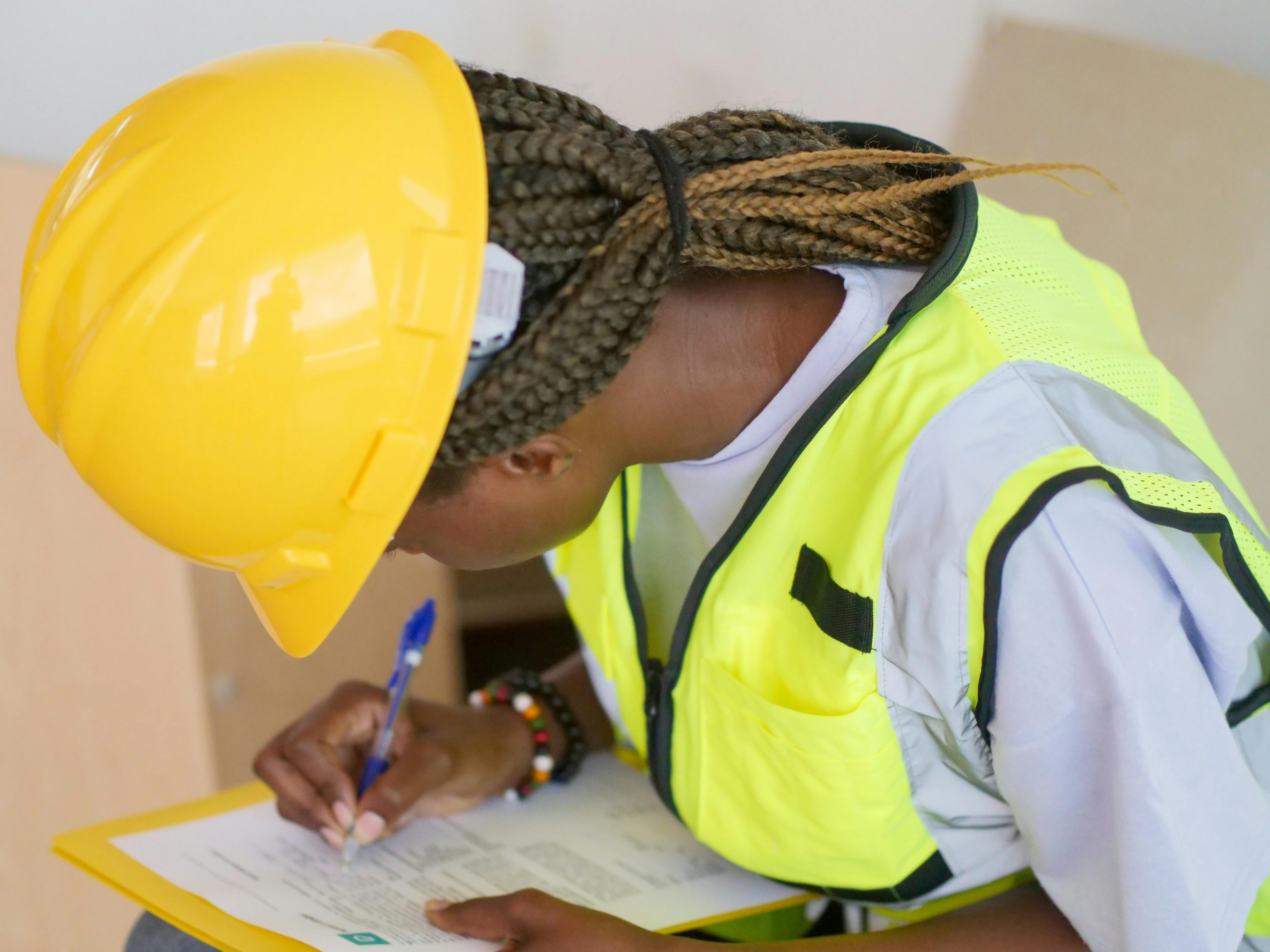 Design, Engineering & Project Management A female engineer in PPE writing on a clipboard at a construction site.